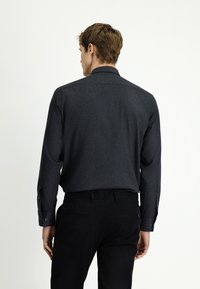 Ciemnoszara koszula z subtelną fakturą, zapinana na guziki, z kołnierzykiem i długimi rękawami. Czarne spodnie z tylnymi kieszeniami.