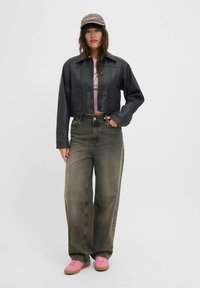 Veste en cuir noire courte avec deux poches avant, associée à un jean ample taille haute vert olive et des baskets rose clair. Casquette marron.