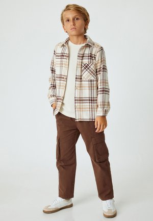 Rutete flannel skjorte i creme, brun og beige, lagdelt over en let sweater, parret med brune cargo bukser og hvide sneakers.