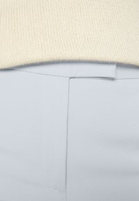 Zbliżenie na pas jasnoniebieskich spodni z ukrytym zamkiem błyskawicznym oraz kremowy sweter z dzianiny włożony do środka.