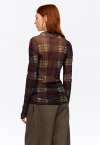 Koszula z długim rękawem wykonana z przezroczystego materiału z wielokolorowym wzorem w kratę w odcieniach zieleni, czerwieni i czerni. Prosty, dopasowany fason.