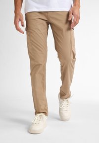Beige cargo bukser med sidelommer, lavet af letvægtsstof. Glat tekstur, tapered pasform, parret med hvide sneakers.