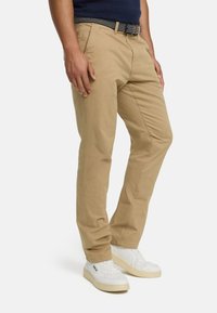 Beige cotton chinos with a straight fit, featuring front pockets and a textured black and white belt. Paired with white sneakers.