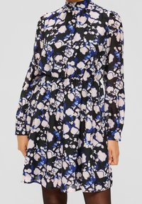  långärmad klänning med hög krage, prydd med svart tyg med ett blommönster i blått och rosa. Elastisk midja, knälång.
