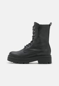 Stivaletto in pelle nera alla caviglia con design a lacci, punta tonda, suola in gomma spessa e linguetta sul tallone. Presenta occhielli in argento.