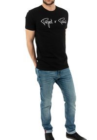 Camiseta de algodón negra con texto en blanco que dice "Project x Paris," combinada con jeans azul claro y zapatillas negras para un look casual.