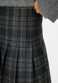 Jupe à carreaux noir et gris avec des plis et une fermeture éclair à la taille, fabriquée dans un tissu lisse au design structuré.