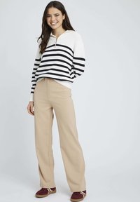 Le pull présente une base crème avec des rayures horizontales marines, un col zippé et une coupe décontractée. Le pantalon est beige, taille haute et à jambe large.