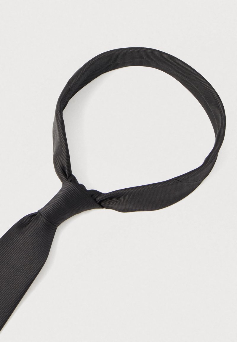 Cravatta nera di seta, tessuto liscio, forma stretta, annodata a nodo, con un motivo a righe sottili. Adatta per occasioni formali.