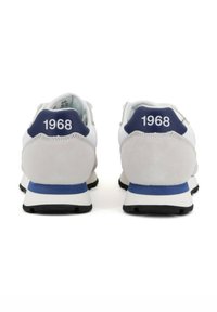 Zapatillas deportivas blancas con un talón de gamuza gris, detalles en azul y el número "1968" en la parte trasera. Suela de goma texturizada para un mejor agarre.