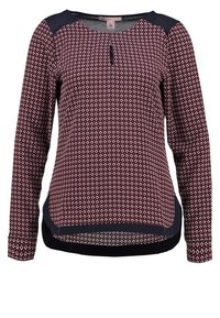Blouse bordeaux à manches longues avec petit motif losange blanc, empiècements bleu marine aux épaules et bordure bleu marine à l’ourlet et à l’encolure.