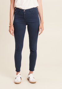 Slim-fit marineblauwe jeans met vijf zakken, een ritssluiting aan de voorkant en een knoopsluiting. Gepaard met witte sneakers met zwarte accenten.