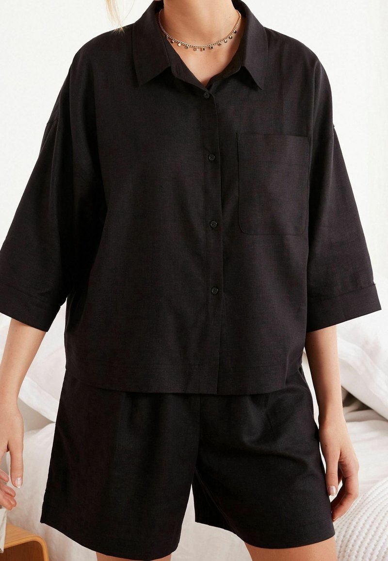 Czarna, krótko-sleeve koszula z guzikami i kieszonką, w komplecie ze spodniami szortami w tym samym kolorze. Materiał ma teksturowane wykończenie. Prosty, luźny krój.