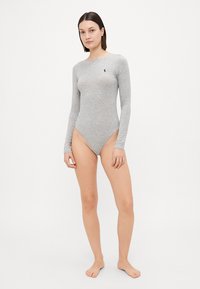 Pilkas ilgomis rankovėmis bodysuit'as, su prigludusia išvaizda ir aukštai iškirptomis kojomis. Ant krūtinės yra mažas mėlynas logotipas. Lygus, tamprus audinys.