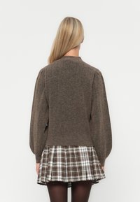 Brun strikkegenser med puffede ermer, sammen med et rutete skjørt med brune, hvite og svarte striper langs kanten.
