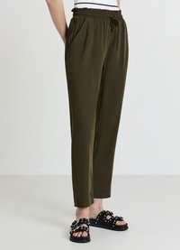 Pantaloni verde oliva leggeri con cintura elastica e coulisse, dotati di tasche laterali e design a gamba affusolata. Sandali neri decorati con dettagli.