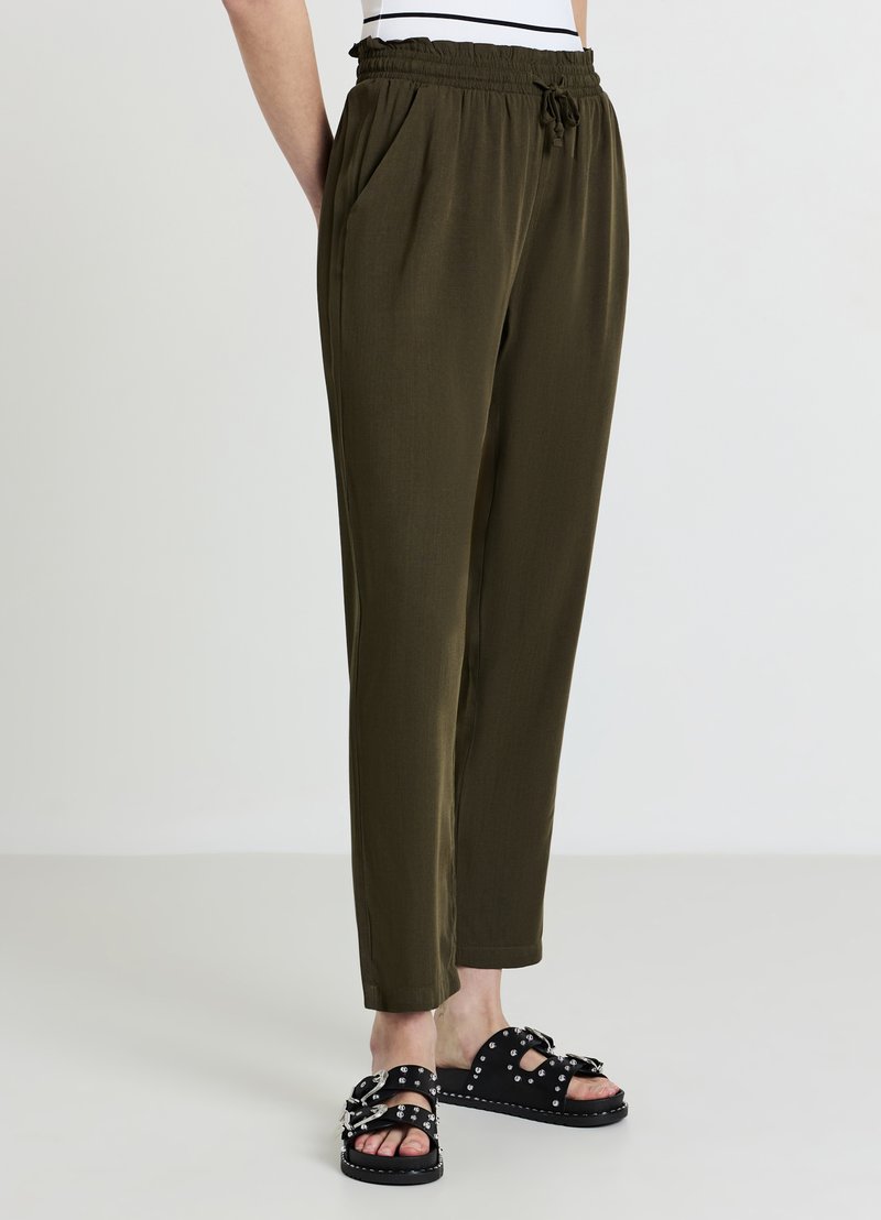 Pantaloni verde oliva leggeri con cintura elastica e coulisse, dotati di tasche laterali e design a gamba affusolata. Sandali neri decorati con dettagli.