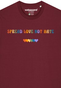 Maroon Baumwoll-T-Shirt mit mehrfarbigem Text, der "SPREAD LOVE NOT HATE" (VERBREITE LIEBE, NICHT HAß) sagt, sowie einer Reihe bunter Herzformen darunter.