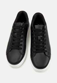 Baskets en cuir noir avec des semelles en caoutchouc blanc, caractérisées par des orteils ronds, des lacets plats noirs et de subtiles coutures sur la surface supérieure.