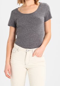 Šedé tričko s krátkým rukávem a kulatým výstřihem, vyrobené z měkké látky, spárované s bílými high-waisted džíny s knoflíkovým a zipovým zapínáním.