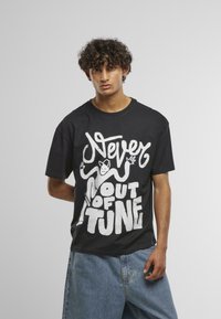 Fekete pamut póló nagy fehér grafikával, melyen a "Never out of tune" felirat szerepel egy rajzfilmfigurával a középpontban. Rövid ujjak, laza szabás.