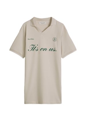 Beżowa koszulka polo z krótkim rękawem z zielonym napisem "It's on us." i logo Marc O'Polo na piersi, z małym kołnierzykiem i dekoltem w serek.