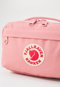 Fjällräven Kånken roze tas met dubbele ritsen, textuurstof en centrale logo patch met een ontwerp van een rode vos. Compacte en rechthoekige vorm.