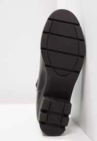 Czarne botki za kostkę z teksturowaną gumową podeszwą z rowkami dla lepszej przyczepności, okrągłym czubkiem i minimalnymi detalami na górze. Rozmiar 37.