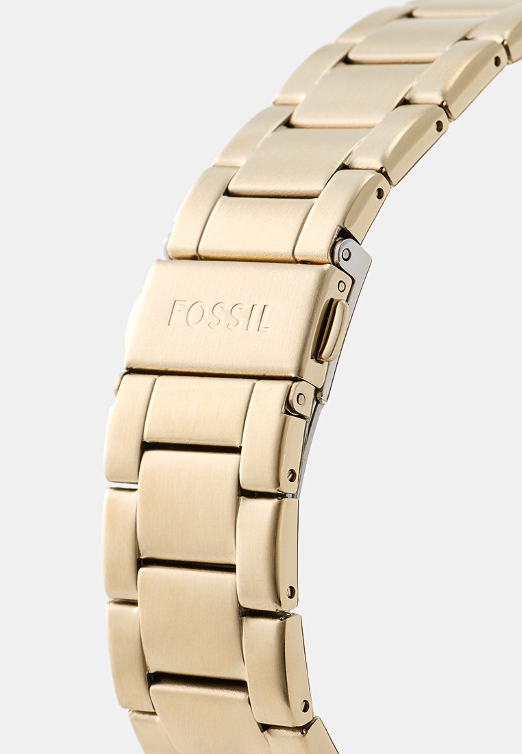 Bracciale in metallo tono oro per orologio con chiusura incisa "FOSSIL", dotato di meccanismo di rilascio a pulsante.