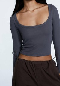 Grå ribbad långärmad topp med en bred rund halsringning och figursydd design. Matchad med löst sittande bruna byxor med snörning.