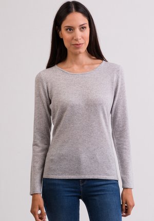 Grijze langwerpige top met lange mouwen van zachte stof, ronde halslijn en slim fit, gecombineerd met blauwe jeans. Eenvoudig ontwerp zonder zichtbare patronen of accenten.