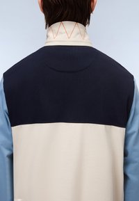 Svetr ve dvou tónech s béžovou dolní polovinou, námořnickou horní částí a světle modrým rukávem. Límec zdobí oranžové cik-cak prošívání.