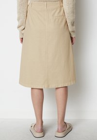 Beige Baumwollrock knielang mit geradem Schnitt, Rückentaschen-Detail und dezentem gesticktem Saum, kombiniert mit hellbeigen Slippern.