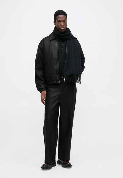 Black leather bomber jacket, black polo shirt, matching wide trousers, and a fringed black scarf. Solid color, minimal texture, sleek design.