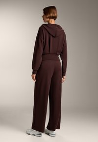 Brązowa bluza z kapturem, szerokimi rękawami i dopasowanymi szerokimi spodniami. Materiał wydaje się miękki. Buty są jasnoszare z akcentami.