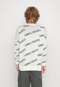 Weißer Strickpullover mit wiederholtem schwarzen Textmuster "CARLO COLUCCI", mit gerippten Bündchen und Saum, von hinten gezeigt.