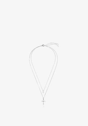 Collier double chaîne en argent avec une petite gemme ronde sur la chaîne supérieure et un pendentif croix orné de cristaux sur la chaîne inférieure.