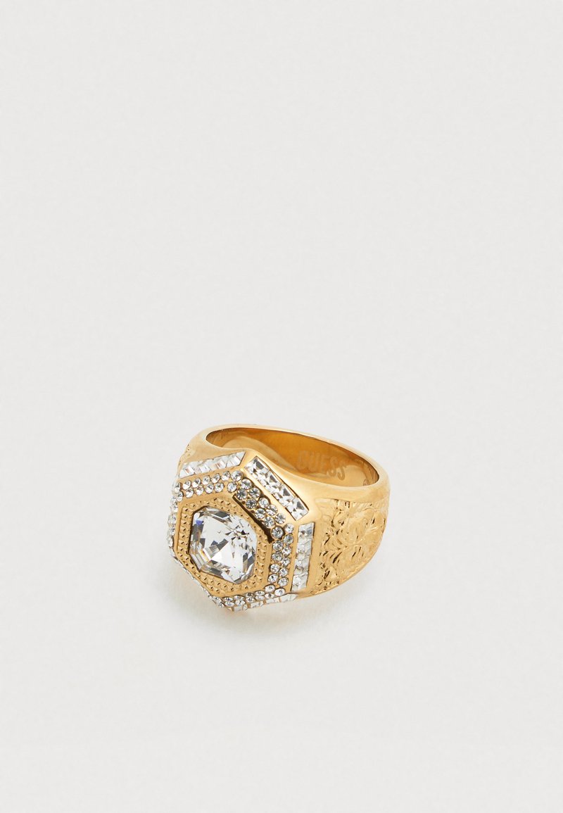 Anello d'oro con design esagonale, caratterizzato da una grande pietra centrale trasparente e da piccole pietre trasparenti circostanti, fascia testurizzata con motivi floreali.