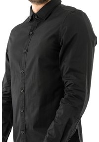 Camisa negra de botones con tejido suave, de mangas largas, con un cuello puntiagudo y botones en la parte delantera, con un logo sutil en el pecho.