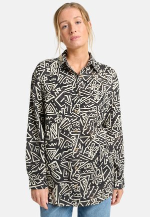Camisa negra con patrones abstractos blancos, con botones en la parte delantera, mangas largas y cuello. El material parece texturizado, ofreciendo un aspecto casual.