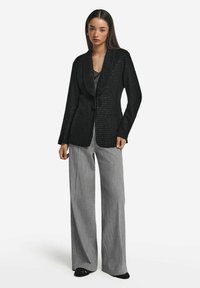 Svart, texturerad blazer med knytning framtill, med långa ärmar och avslappnad passform. Matchas med grå, vida byxor.