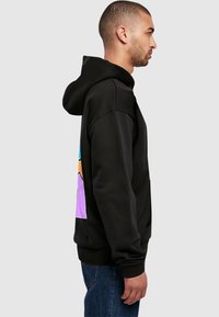 Schwarze Kapuzenjacke mit einem bunten Bergdesign auf der Rückseite, aus Baumwollmischgewebe gefertigt, mit einer Fronttasche und gerippten Bündchen.