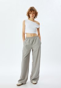 Top court blanc à une épaule associé à un pantalon large gris clair, doté d'une taille élastique et d'un tissu lisse et léger.