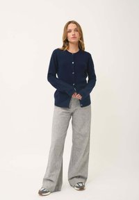 Marineblauwe cardigan met ronde hals, lange mouwen, knoopsluiting en geribbelde manchetten, gecombineerd met lichtgrijze wijde broek.