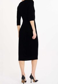 Robe midi en velours noir avec manches trois-quarts, coupe cintrée et texture lisse, associée à des escarpins noirs pointus.
