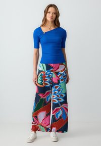 Blauw geribd T-shirt met korte mouwen en een asymmetrische halslijn, uitgerust met knoopdetail, gecombineerd met wijde, kleurrijke bloemenprintbroeken.