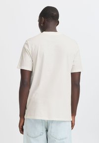 Ljusbeige kortärmad t-shirt med rundad hals, tillverkad av mjuk bomull. Avslutad med rak fåll och utan synliga mönster eller grafiska tryck.