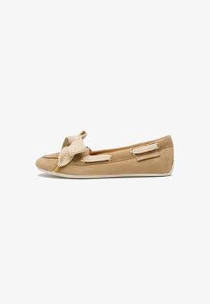 Mocassin plat en suede beige avec un nœud texturé à l'avant, des accents dorés et une semelle en caoutchouc blanc. Comprend un laçage décoratif sur les côtés.