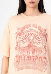 Camiseta oversized de color durazno hecha de una tela suave, con un atrevido diseño gráfico rojo de un sol, una montaña y el texto "Good Vibes All Around".