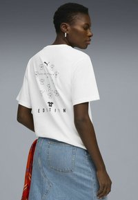 T-shirt blanc à manches courtes avec un imprimé graphique de chemises et du texte dans le dos. Tissu en coton doux, coupe décontractée.